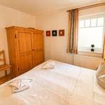 Schlafzimmer mit Bett, Holzschrank und Fenster mit Vorhängen.