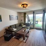 Wohnzimmer mit Sofa, Couchtisch und Blick auf Balkon. Wandbilder und Holzboden.