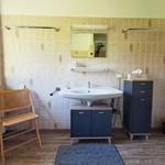 Badezimmer mit Waschbecken, Spiegel, Stuhl und Schrank.