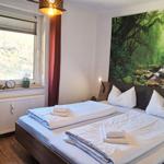 Schlafzimmer mit Bett, Fenster und Wandbild. Auf dem Bett liegen Handtücher.