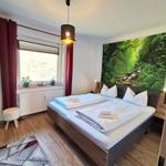 Schlafzimmer mit Doppelbett, Wandbild Wald, Fenster mit Blick, Holzboden und Deckenleuchte.