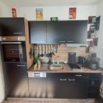 Küche mit schwarzen Schränken, Edelstahlspüle und Kochfeld. Dekorative Flaschen und Poster an der Wand.