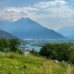 Panoramablick auf See und Berge mit grüner Wiese im Vordergrund.