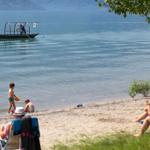 Strand mit Kindern, Erwachsenen und einem Boot im Wasser.