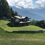 Haus auf grüner Wiese mit Bergblick und umliegenden Bäumen.