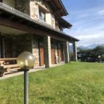 Steinhaus mit Holzveranda und Garten. Berglandschaft im Hintergrund.