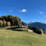 Haus auf grüner Wiese mit Blick auf schneebedeckte Berge und Wald.