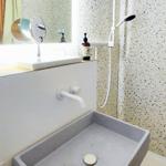 Bad mit Dusche, Waschbecken und Spiegel. Wand mit Terrazzopflaster.