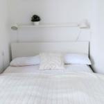 Ein Bett mit weißer Bettwäsche, Kopfteil und Nachttischlampen an der Wand.