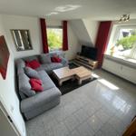 Wohnzimmer mit grauem Sofa, roten Kissen, Holztischen und Fenstern mit roten Vorhängen.