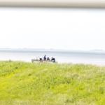 Zwei Personen sitzen am Ufer eines Sees mit Grasland im Vordergrund.