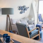 Wohnzimmer mit Sofa, Sessel und Balkonansicht. Holztisch, Stehlampe und Wanddekoration.