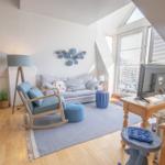 Wohnzimmer mit Sofa, Schaukelstuhl und TV. Holzboden und große Fenster.