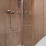 Dusche mit Glaswand und Handbrause, Wandverkleidung aus hellbraunen Fliesen.