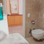 Badezimmer mit Toilette und Blick in den angrenzenden Raum mit Waschbecken und Spiegel.