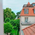 Rotes Dach mit Dachfenstern und Balkon. Grüne Bäume und Gärten im Hintergrund.