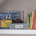 Bookshelf with beach theme and wooden box labeled Strandgut.