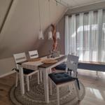 Dining area with table, chairs, and pendant lights. Round rug and window with curtains.