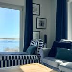 Wohnzimmer mit Sofa, Sitzbank und Blick aufs Meer durch Fenster.