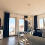 Wohnzimmer mit Sofa, Couchtisch und TV. Große Fenster mit Blick auf das Meer.