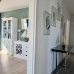 Hallenflur mit Bildern, Tisch und Modellboot. Links Wohnbereich mit Bücherregal und Balkon.