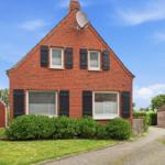 Red brick house with black shutters and satellite dish under blue sky.