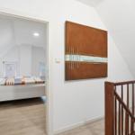 Bedroom with bed and windows, wall art and wooden railing visible.