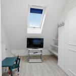 Bedroom with skylight, TV, and childrens table. White walls and wooden floor.