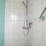 Shower with showerhead, handheld shower, and holder on white tiles.