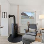 A living room with a gray armchair, wooden floor, and a black wood stove.