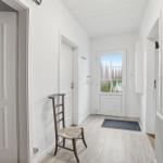 Hallway with white walls, wooden floor, and door to outside area.