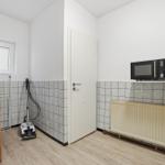 Kitchen with microwave, radiator, and vacuum cleaner. Tiled wall and wooden floor.