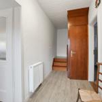 Hallway with wooden stairs, door, and chair. Kitchen visible on the left.