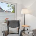 A gray armchair with a cushion is near a window with blinds. A floor lamp stands beside it.