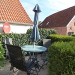 Garden with table, chairs, and closed umbrella between hedges and houses.