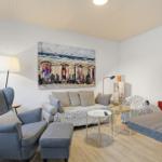 Living room with sofa, armchair, and wall art. TV and tables are present.