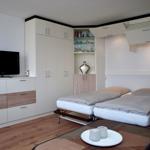 Zimmer mit Bett, Schränken und Fernseher. Holzfußboden und moderne Einrichtung.