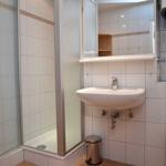 Badezimmer mit Dusche, Waschbecken und Toilette. Weiße Fliesen und Spiegelschrank.
