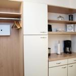 Kleiderkammer mit Kleiderständer und integrierte Küchenzeile mit Kaffeemaschine.