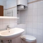 Badezimmer mit Waschbecken, Toilette und Spiegel. Wandfliesen und Heizkörper sichtbar.