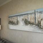Ein Wandbild zeigt einen Strand mit Holzzaun und Gras. Links steht eine Stehlampe.