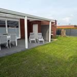 Terrace with table, chairs, and loungers. Lawn and fence in the background.