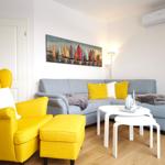 A living room with a gray sofa, yellow armchair, and wall art of sailboats.