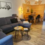 Wohnbereich mit Sofa, Esstisch und Küchenbereich. Holzdielenboden und Wanddekoration.