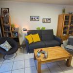 Wohnzimmer mit grauem Sofa, Holztisch und Bücherregal. Fenster und Heizung sichtbar.