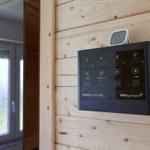 Sauna-Kontrollgerät an Holzwand mit Temperaturanzeige und Fenster im Hintergrund.