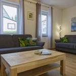 Zwei graue Sofas, Holztisch, Fenster mit Vorhängen, Wandbilder