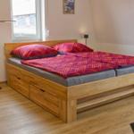 Doppelbett mit Holzrahmen und integrierten Schubladen, rote Bettwäsche, Fenster und Stehlampe.