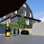Außenbereich mit Tisch, Stühlen und einer Flasche Prosecco unter einem Sonnenschutz.