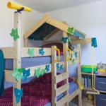 Ein Kinderzimmer mit einem hölzernen Doppelbett, Spielzeug und einem Regal mit Büchern und Kisten.